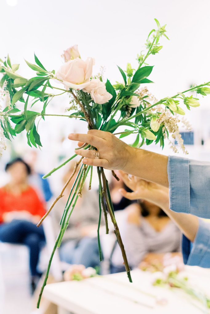 Amy from Amy Nicole Floral holds a small bouquet of flowers in front of her for her students to see as an example of what florists do when answering the question: What is a Florist?