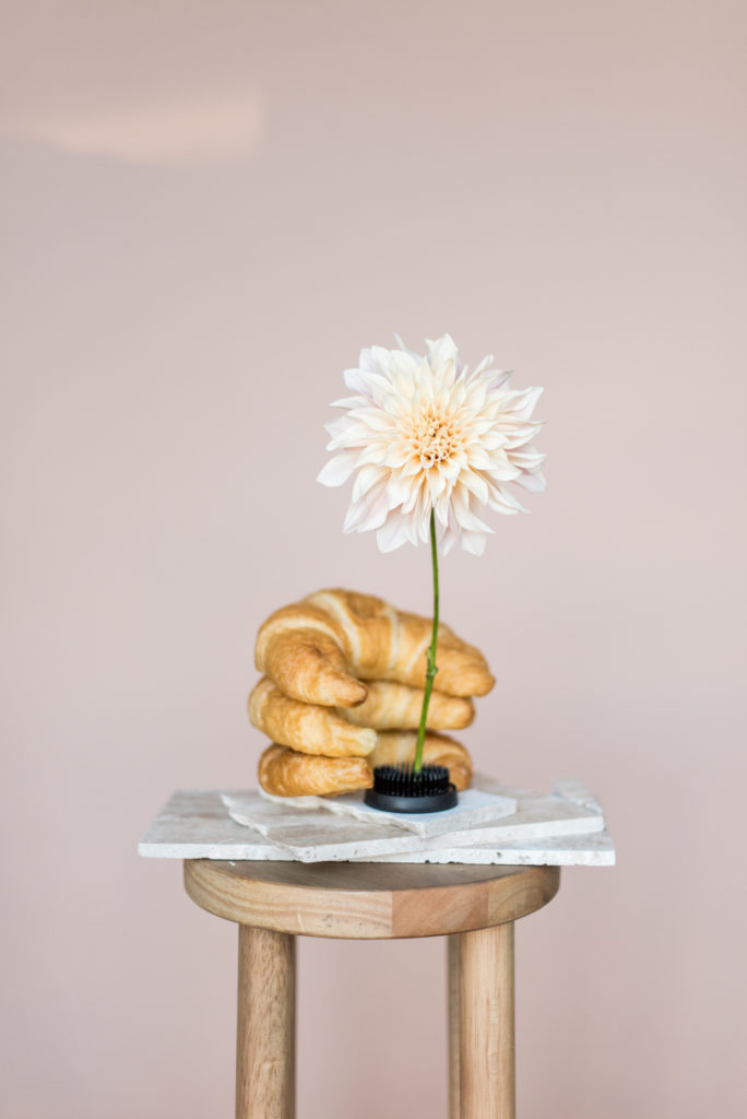 An image of a pile of croissants with a daisy resting on a stool