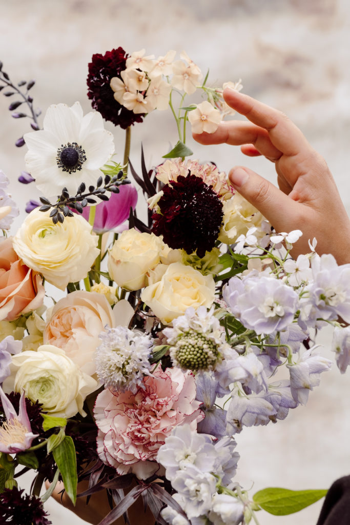 Close-up photo of an elegant floral arrangement with a hand touching one of the flowers; photo by @karenobrist