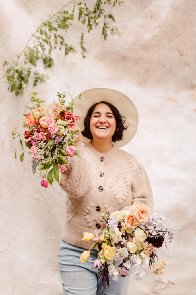 Amy from The Floral Coach smiles as she holds up two floral arrangements from her floral arrangement class; photo by @karenobrist
