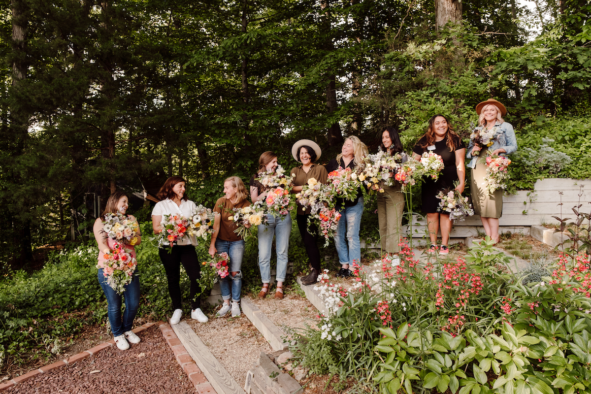 Amy Balsters from the Floral Coach laughs along with her student florists as they stand in a line and showcase their floral arrangements