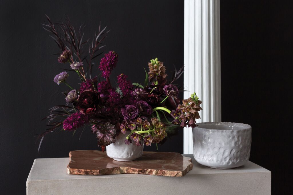 The Floral Coach®, Dark pink hyacinths serve as line flowers in this moody arrangement with fritillaria, lisianthus, ranunculus, begonia, and agonis. Design for Accent Decor. 